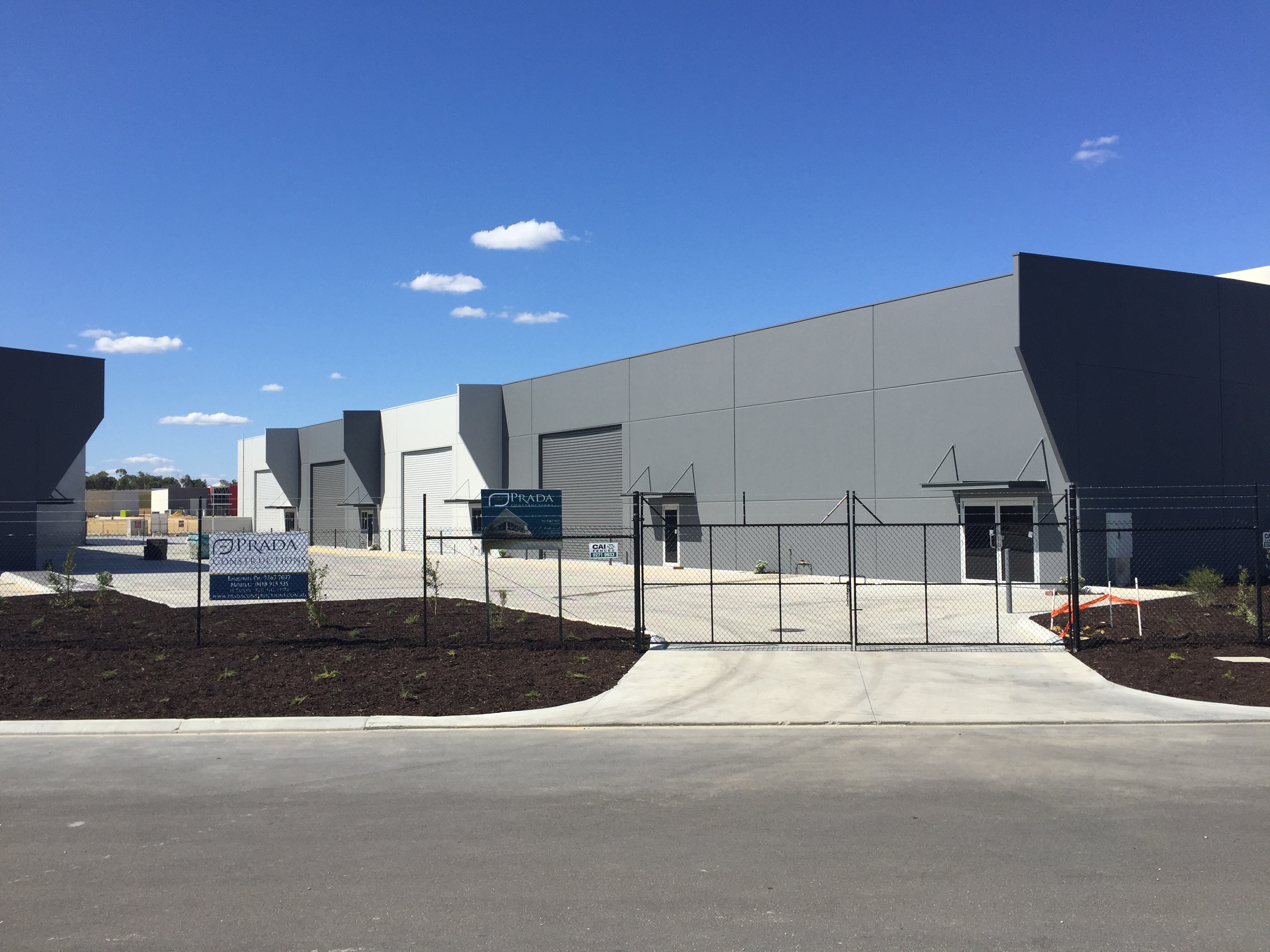 Exterior shot of securely fenced commercial warehouse units, painted in grey and white