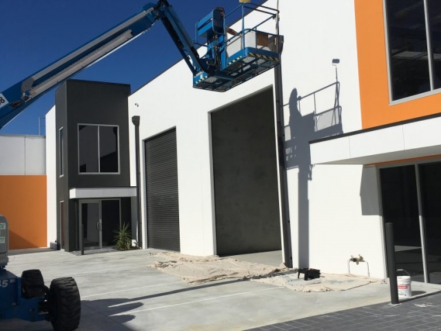 Blue cherry picker parked in front of newly painted commercial warehouse unit finished in white and orange