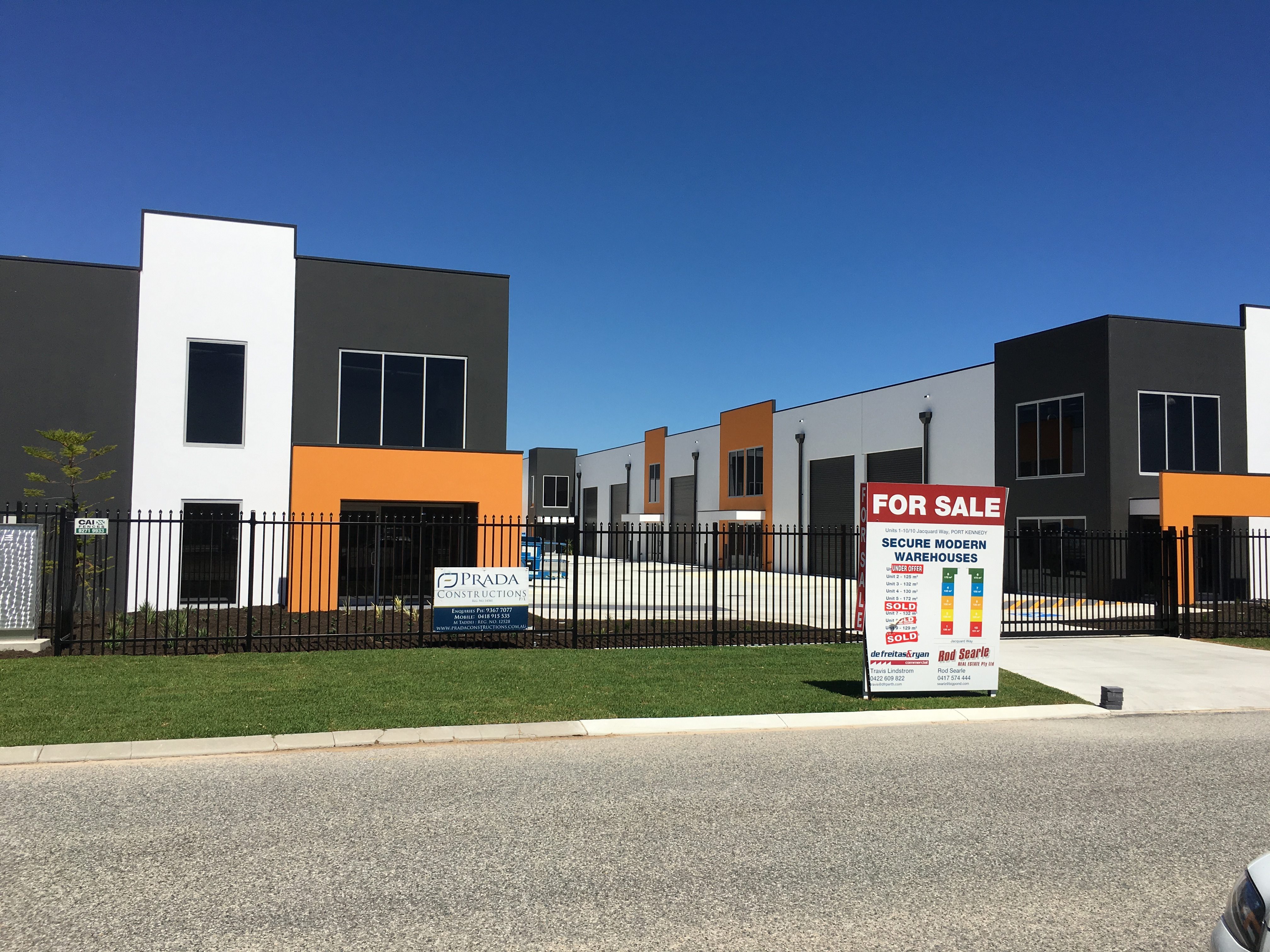 Exterior shot of fenced, modern warehouse units, finished in dark grey, orange and white