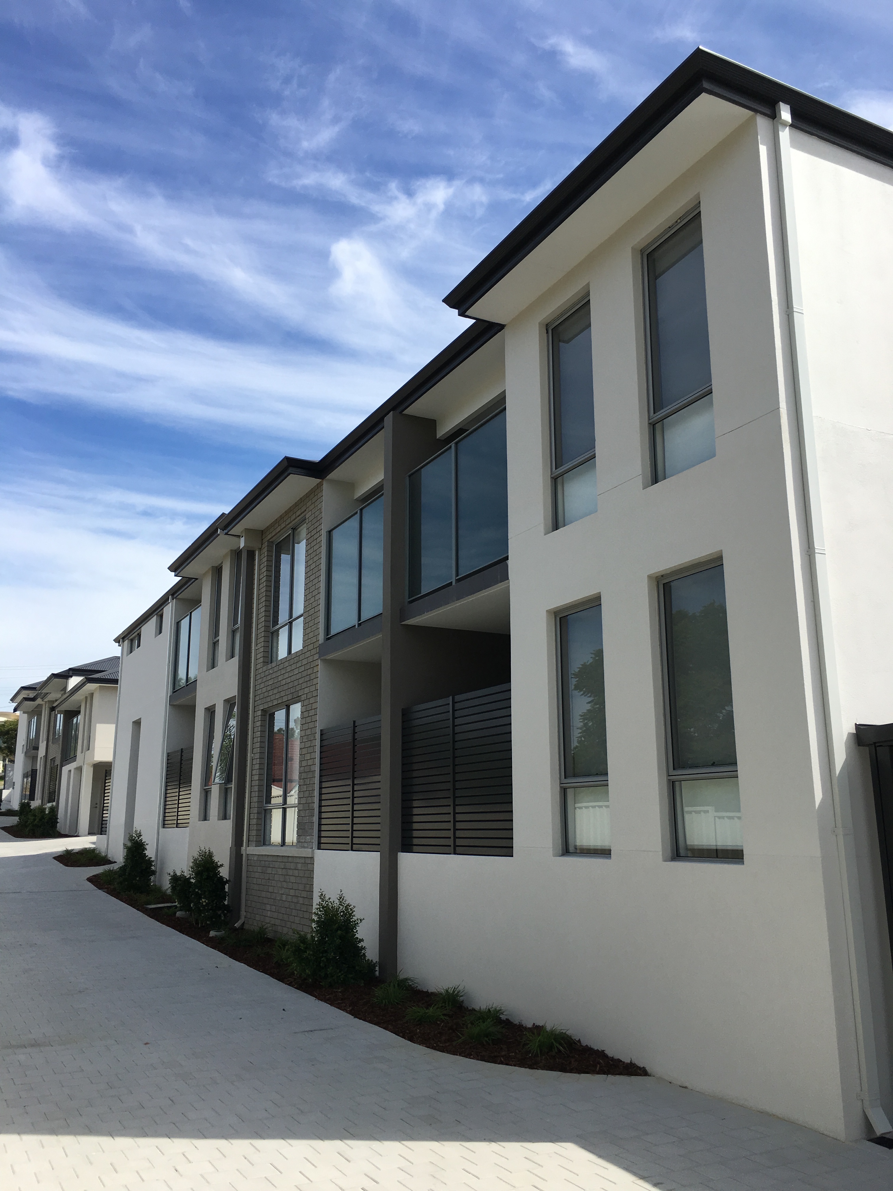 Exterior shot of large multi-unit complex painted in light grey and finished with dark grey and brick accents