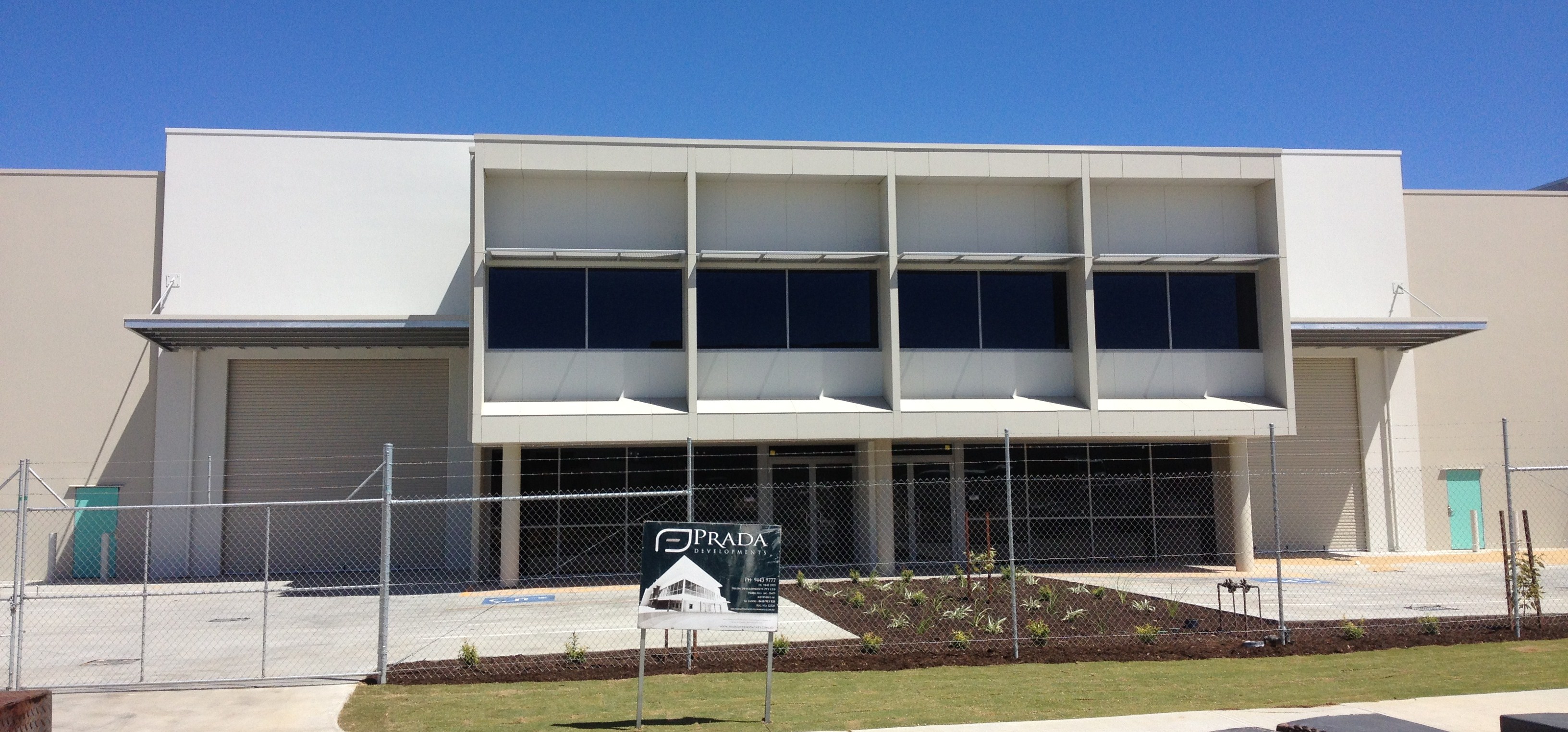 Exterior shot of large commercial warehouse office painted in cream and surrounded by a wire fence