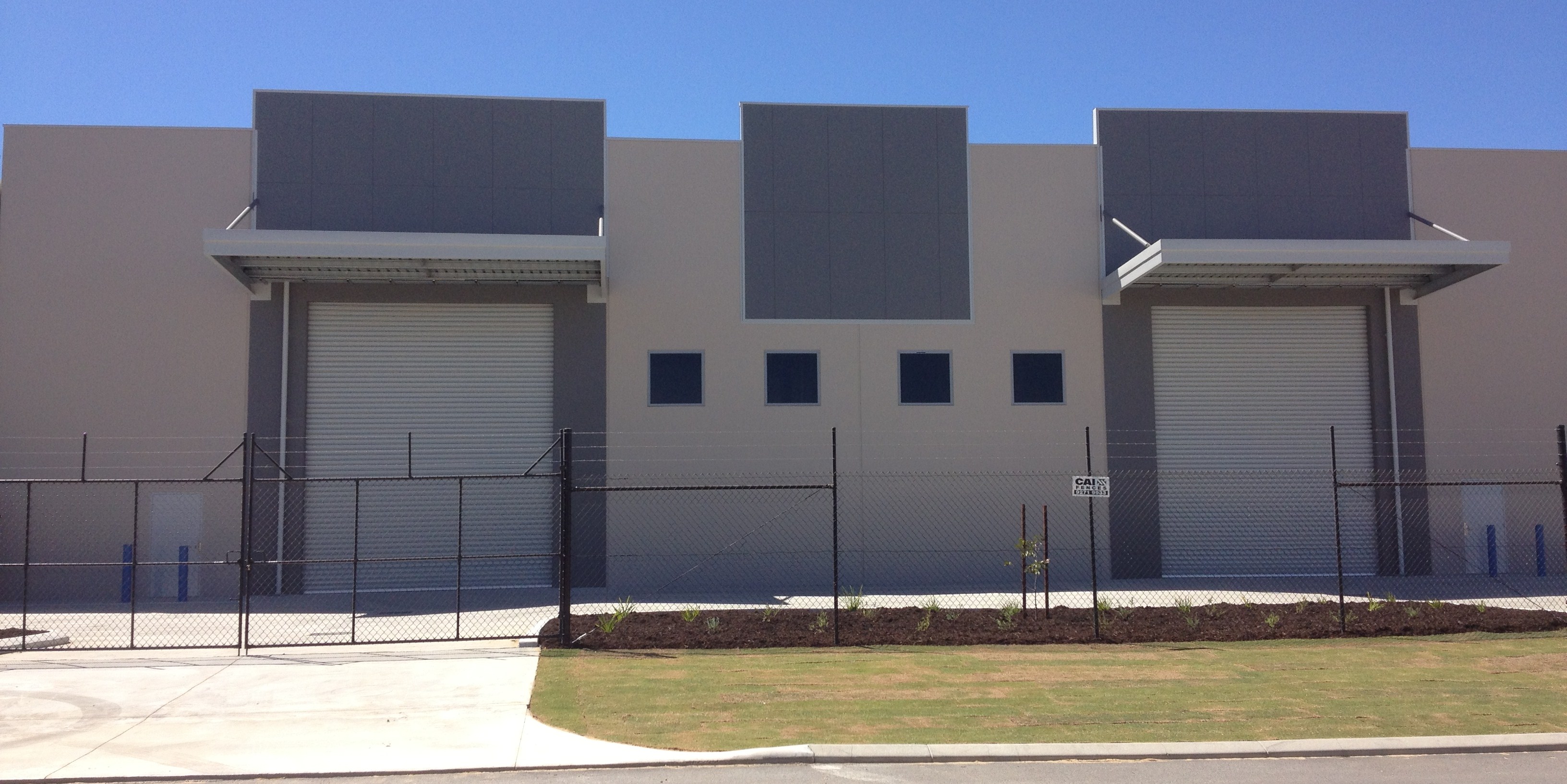 Exterior of large fenced commercial warehouse, painted in light grey with dark grey accents