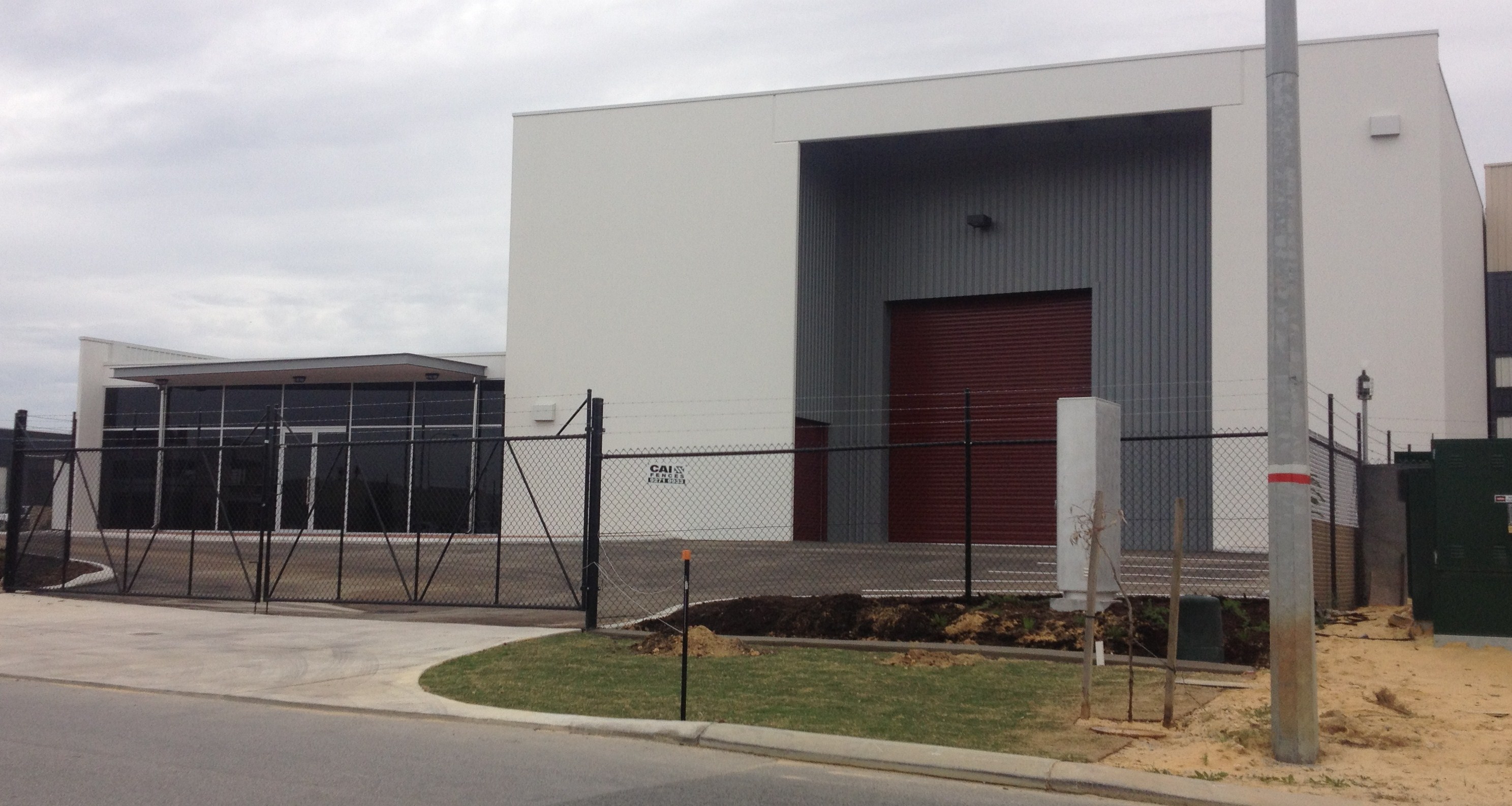 Exterior of large commercial garage and office, painted in grey and maroon and features a security fence