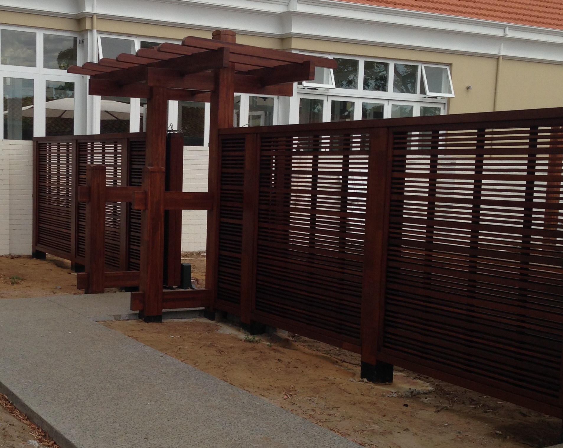 High residential fence and pergola painted in brown stain
