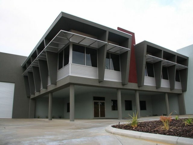 Exterior paint job of large commercial warehouse office, finished in grey with red accents